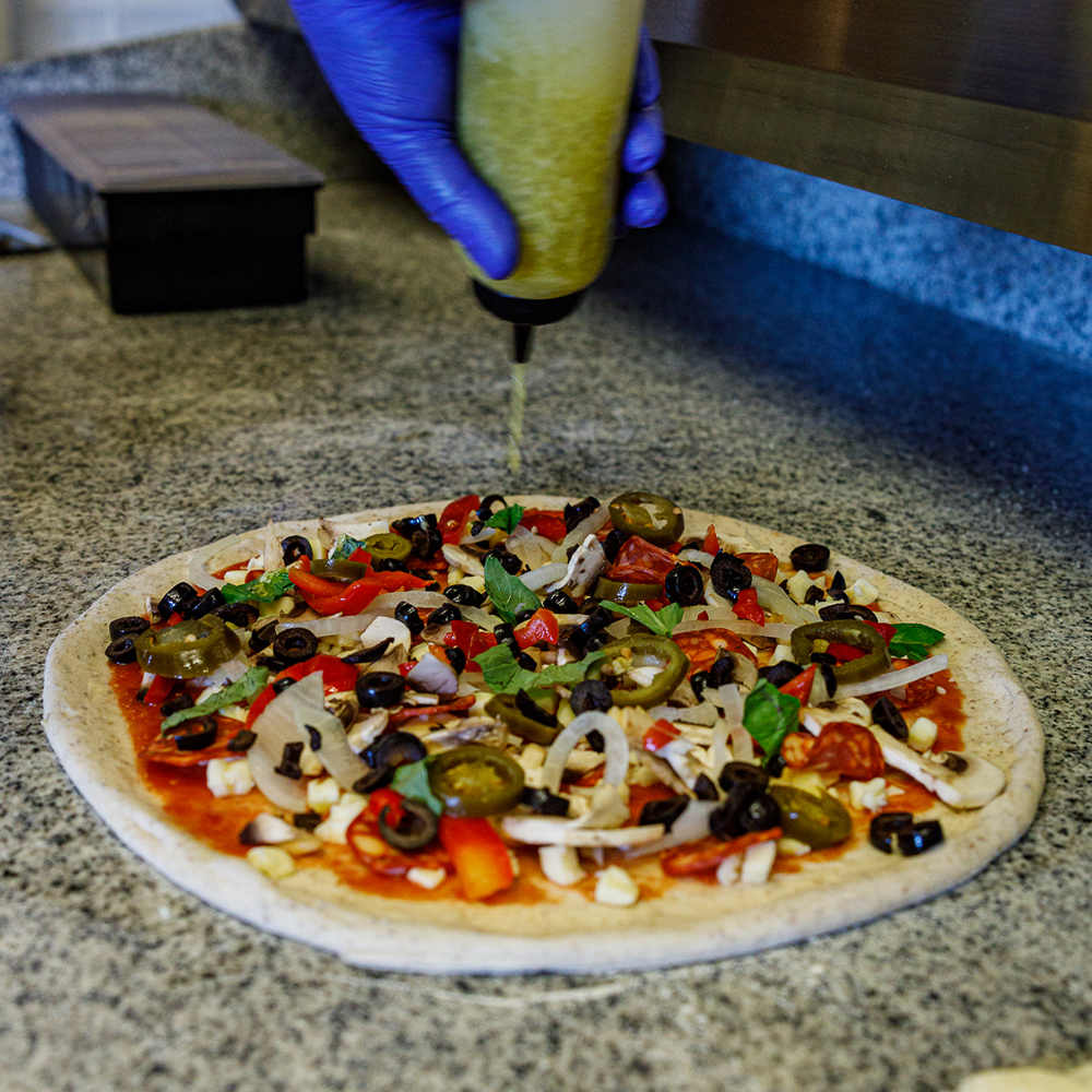 Pizza base being topped with ingredients and sauces